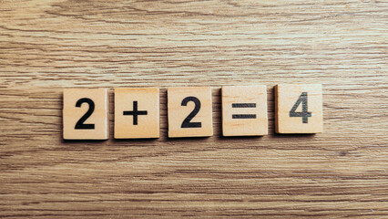 Fototapeta premium Simple addition math equation two plus two equals four using wooden number tiles on wood background