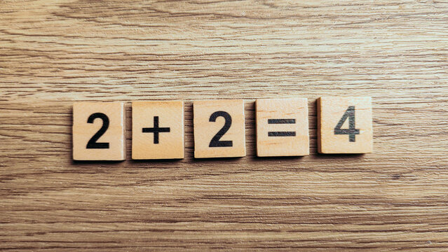 Simple addition math equation two plus two equals four using wooden number tiles on wood background