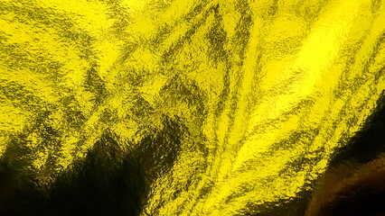 Close up of crumpled yellow gold foil paper texture providing a shimmering metallic background for...
