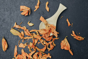Dried orange flower petals scattered on dark surface with wooden scoop