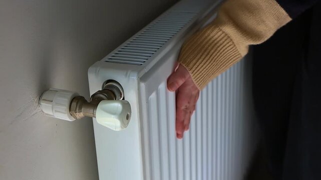 Close-up of a hand adjusting the temperature on a radiator thermostat, regulating home heating for energy efficiency.