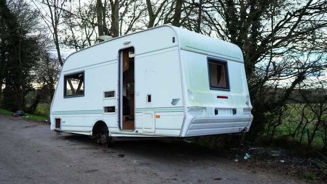 Deserted roadside caravan deteriorating under long term neglect exposure. Illegal occupation forming unsanitary shelter conditions amid rural surroundings. Social crisis unfolding as abandoned mobile