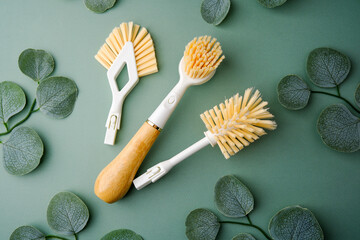 Three cleaning brushes with green leaves on a green background.