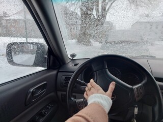 Winter driving in Germany seen from inside the car. Snow-covered streets, icy windshield, and driver&rsquo;s hand on the steering wheel reflect everyday urban transport in cold weather.
