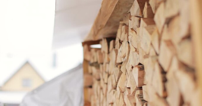 Neatly stacked pile of cut firewood arranged under protective roof. Firewood pile.