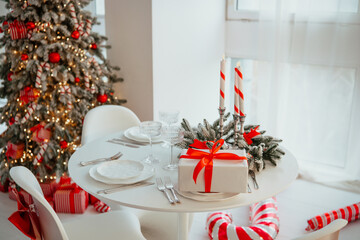 Christmas dinner table setting with festive decor, candles, and gifts near a decorated tree