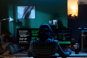 Young Asian woman sitting at desk working on multiple computer monitors with code displayed, analyzing data and programming in dark office environment at night