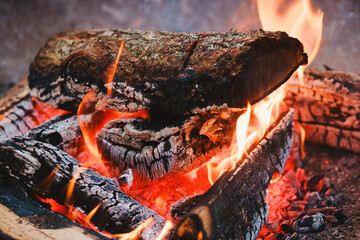 Wood logs burning brightly with fiery orange flames and hot red embers creating warmth outdoors