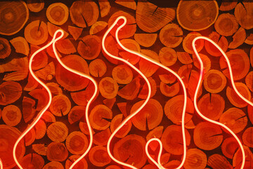 Bright glowing neon tubes form a flame pattern on a textured wall of stacked round wood pieces