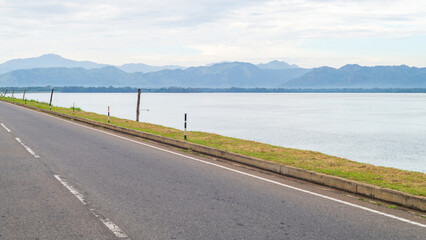 Lakeside road along the edge of Udawalawe Reservoir in Sri Lanka. Bordered by grassy embankments and backed by forested mountains in a tropical dry zone 