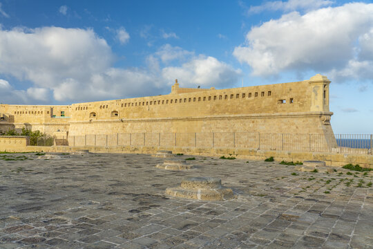 View of Fort St Elmo and the National War Museum across the landscape, bathed in warm sunlight under a sky dotted with fluffy clouds, Valletta, Malta.