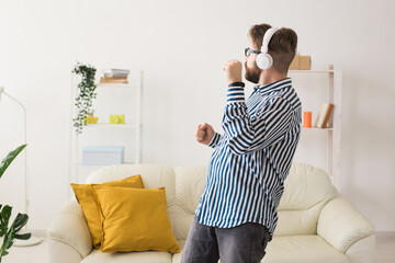 Man dancing while listening to music with headphones in living room. Personal entertainment, audio enjoyment, and expressive movement inside home interior.