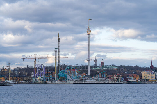 View of amusement park rides punctuate the skyline against a backdrop of muted blue waters and a cloudy sky, a tranquil yet vibrant scene, Stockholm, Stockholm County, Sweden.