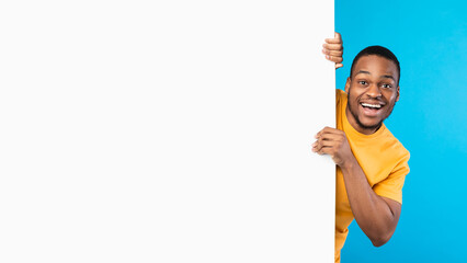 Great Offer Advertisement. Excited African American Man Posing With Big White Poster Looking Smiling To Camera Over Blue Studio Background. Bright Ad Banner With Copy Space. Mockup, Panorama