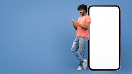 A man stands next to a large blank screen while holding a mobile device. He appears to be engaged...