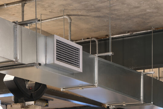 Metal HVAC ventilation duct suspended from a concrete ceiling, showing industrial air distribution system inside a modern building.