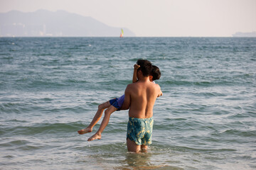 Man carrying the child in sea waves. Concept of water rescue, family holiday and leisure on the beach