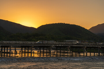 View of a bridge stretching across a river, silhouetted against the setting sun as cars traverse the span, casting shimmering reflections, Kyoto, Kyoto, Japan.