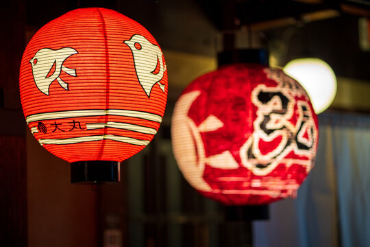 View of vibrant red paper lanterns adorned with traditional Japanese script and bird motifs glow warmly against the soft light, Kyoto, Kyoto, Japan.
