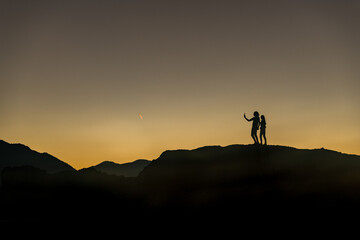 View of silhouetted figures stand atop the rugged peaks, bathed in the warm glow of the setting sun, casting long shadows across the Thessaly landscape, Trikala, Thessaly, Greece.