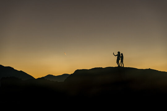 View of silhouetted figures stand atop the rugged peaks, bathed in the warm glow of the setting sun, casting long shadows across the Thessaly landscape, Trikala, Thessaly, Greece.