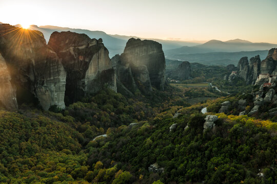 View of sunlight spills over dramatic rock formations and lush green forests in a landscape of ancient monasteries, Trikala, Thessaly, Greece.