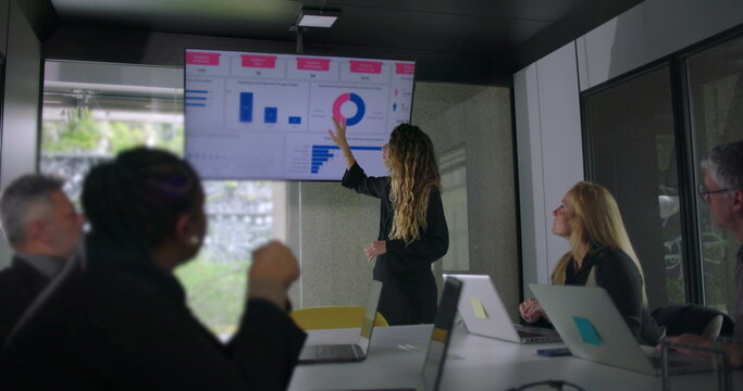 Young woman presenting data chart to colleagues while blonde businesswoman and team members listen attentively in collaborative office meeting - Powered by Adobe
