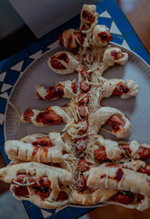 The photo shows a New Year table for children with sausages wrapped in dough served on a plate. Holiday food, kid-friendly meal, festive setting, winter season, close-up view, indoor lighting.