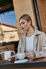 Young blonde woman enjoying coffee at an outdoor cafe terrace on a spring day