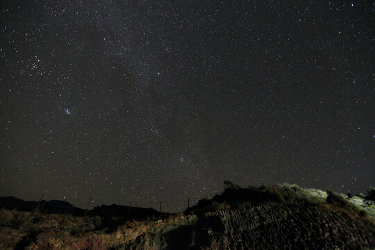 View of a starlit sky ablaze with countless sparkling stars above a dark, rugged landscape with sparse vegetation, Upper Dir, Khyber Pakhtunkhwa, Pakistan.