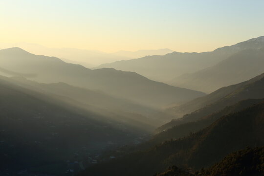 View of golden sunlight piercing through hazy mountain ranges, casting long shadows over the valleys below, Upper Dir, Khyber Pakhtunkhwa, Pakistan.