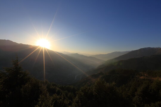 View of the radiant sun bursting over the mountain range casting golden light on the distant valley, Upper Dir, Khyber Pakhtunkhwa, Pakistan.