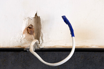 An insulated electrical wire is pulled out of the wall.