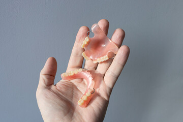 A person holds plastic, nylon, removable dentures in his hand.