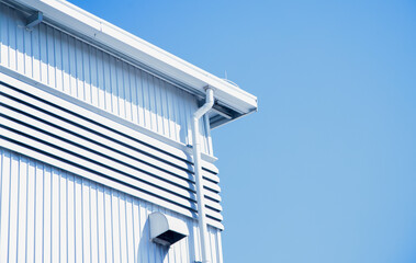 Industrial metal building facade with white gutter and blue sky background,Modern warehouse exterior featuring corrugated metal walls and ventilation slats.