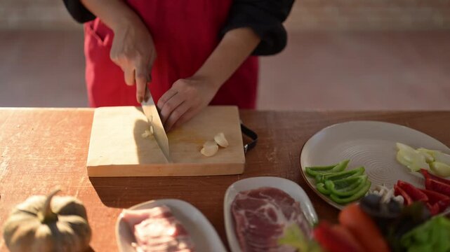 A person is cutting vegetables on a wooden cutting board. There are several different types of vegetables on the cutting board, including peppers, carrots, and squash