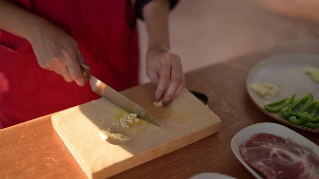 A person is cutting garlic on a wooden cutting board. The garlic is on the cutting board and the knife is in the person's hand