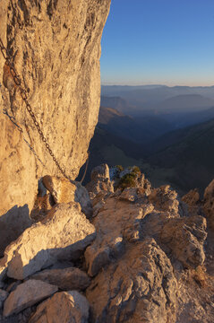 View of a rugged mountain path clinging to a sheer cliff face with safety chains, overlooking a hazy valley under a clear sky, Mala Fatra, Zilina Region, Slovakia.