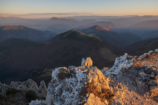 View of frost-covered rocks in the foreground, contrasting with the softer, layered mountain ranges fading into the horizon, Mala Fatra, Zilina Region, Slovakia.