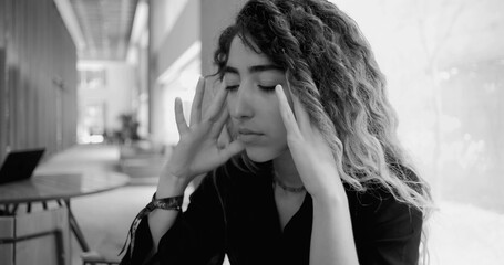 Young woman with eyes closed and fingers on temples, stressed and emotionally drained, monochrome image representing workplace burnout and mental health challenges
