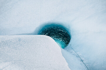 View of an icy cavern mouth glows with an inner turquoise light, surrounded by a landscape of stark white snow and ice, VatnajÃ¶kull National Park, South Iceland, Iceland.