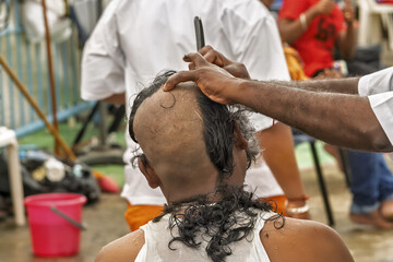 Thaipusam festival in Singapore, showing a devotee undergoing head shaving with a straight razor....