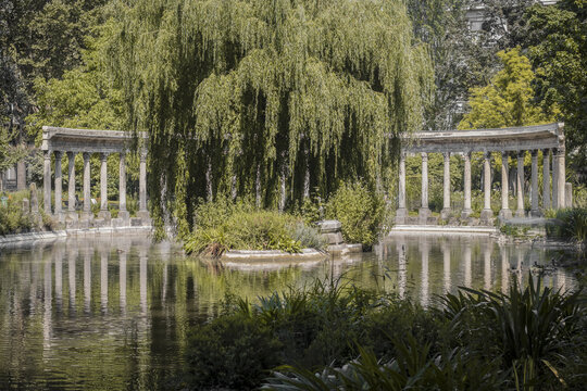 View of tranquil waters mirroring the weathered columns and lush greenery, punctuated by a weeping willow's cascading branches, Paris, &Atilde;Žle-de-France, France.