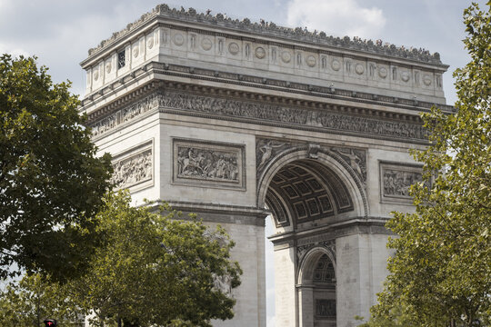 View of the Arc de Triomphe bathed in soft light, framed by vibrant green trees against a cloudy sky, showcasing architectural grandeur, Paris, &Atilde;Žle-de-France, France.