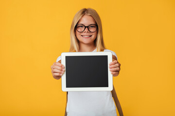 Happy teenager blonde lady schoolgirl in glasses shows tablet with blank screen, recommends new app, isolated on yellow background, free space. Back to school, good website and distance education