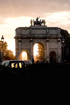 View of the Arc de Triomphe du Carrousel stands silhouetted against a fiery sunset, the golden light piercing through its arches, Paris, &Atilde;Žle-de-France, France.
