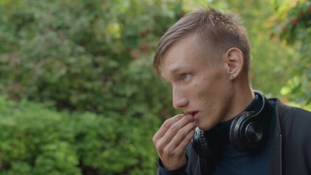 caucasian man with headphones smiling conversationally, animated expressions while nibbling snack and chatting in leafy park setting, scenes include vlogger talking, food taster sampling, storyteller