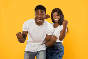 Two young adults stand together with smiles, showing excitement and happiness. They wear casual...