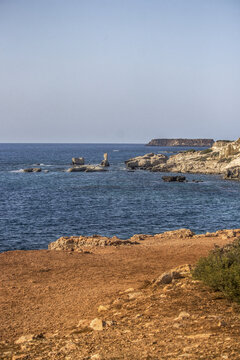 View of the rugged, sun-baked coastline meets the azure sea, where rocky outcrops stand defiant against the relentless waves, Paphos, Paphos, Cyprus.