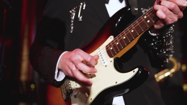Concert view of an electric rhythm guitar player with vocalist and rock band performing in a club, male musician guitarist on stage with audience in crowded concert hall arena, hands on guitar